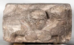 Kubisches Architekturelement mit Relief eines männlichen Kopfes zwischen zwei zurückblickenden Löwen