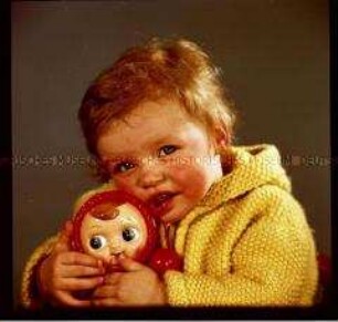 Kleines Mädchen mit Strickjacke und Puppe