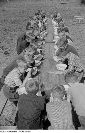 Kinder während des Essens an einer Holztafel im Freien