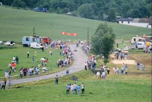 Seifenkistenrennen: viele Leute auf Wiesen beidseitig der Straße, Seifenkisten kommen von Kleinbucha nach Dienstädt