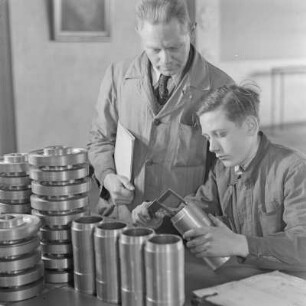 Lehrling bei Borgward misst ein Bauelement, der Ausbilder schaut zu