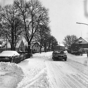 Hauptstraße, Landesstraße L89: Mercedes-Pkw: Häuser, Jägerzaun, parkender Pkw, Gartenhecken, Straßenbäume: links Abzweig Alte Dorfstraße: vorne links zusammengeschobener Schnee: im Winter