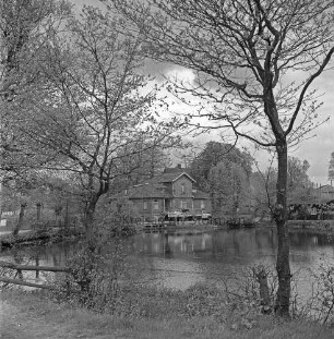 Mühlenteich: vorn Zaun: rechts und links Bäume: rechts Hinweisschild: hinten Mitte zwischen Bäumen Mühle: davor Lkw mit Anhänger: hinten rechts Schuppen