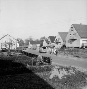 Herrendamm: Neubausiedlung: vorn rechts Sandhaufen: links eingezäunter Garten: in der Mitte Schuljunge: dahinter zwei Lieferwagen: dahinter Einfamilienhäuser: hinten Bäume