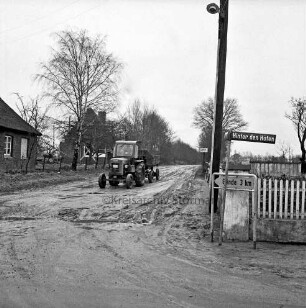 Glinder Weg: rechts Abzweigung Hinter den Höfen mit Straßenschild: dahinter Strommast: links Wohnhäuser mit Bäumen: in der Mitte Trecker