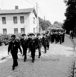Eichede: Amtsfeuerwehrfest des Amtes Mollhagen: Festumzug der Freiwilligen Feuerwehren mit Feuerwehrkapellen: hinten rechts die Feuerwehrkapelle Mollhagen, dahinter die Freiwillige Feuerwehr Eichede: hinten links Bauernhaus und Bäume