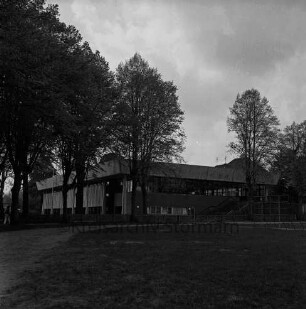 Stormarnhalle: Bürgerpark: vorn Grünfläche mit Bäumen: dahinter Weg und Jägerzaun: hinten rechts Spielplatz mit Klettergerüst