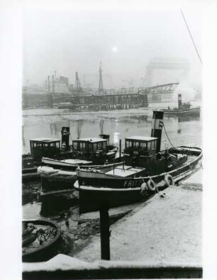 Hamburg. Hafen. Winter. Schlepper liegen im teilweise vereisten Hafenbecken vor Anker. Im Morgennebel die Silhouette der Hafenanlagen