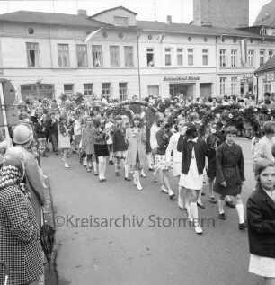Kindervogelschießen: Umzug: Abbiegen von Pferdemarkt in Lübecker Straße: Mädchengruppe mit Blumenbögen, dahinter Jungengruppe mit Blumenstöcken und Fähnchen: an den Straßenrändern Zuschauer: hinten Schlachterei Starck, 30. Mai 1969