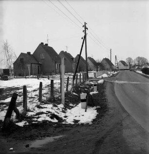 Neubausiedlung: vorn links Wiese mit Zaun: davor Strommast: Winter