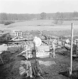 Trave: Spannbetonbrücke: Neubau: am Ufer Holzgerüste für das Setzen der Betonpfeiler: hinten rechts alter Notsteg: hinten Kneeden