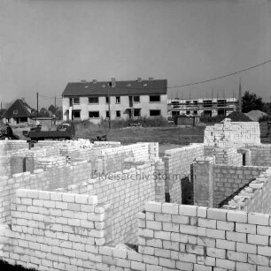 Wohnungsbau: Neubaugebiet Kellerberg-Süd: Wohnblocks im Bau: vorn Grundmauern, hinten rechts Rohbau mit Gerüst: hinten Mitte Block vor Fertigstellung: hinten links Einfamilienhaus: dazwischen unbebautes Gelände mit Sand- und Erdhaufen, VW-Käfer, Baubude sowie landwirtschaftliches Fuhrwerk mit Anhänger