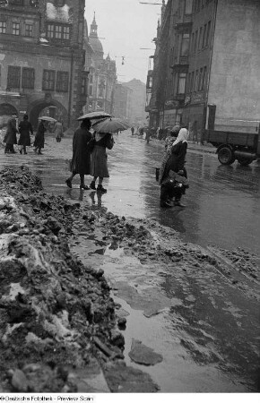 Passanten am Markt im Regen, im Hintergrund das Alte Rathaus
