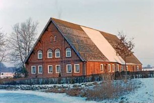 Fischbek: Am Dorfplatz 7: Bauernhaus aus Backstein: Giebelseite Wohntrakt mit Gesims, Lisenen, in Giebel Bogenfenster: Traufseite, links Wohntrakt mit Tür, dahinter Sprung, Wirtschaftstrakt: vorne Feldsteinmauer, Hecke