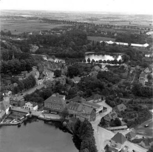 Claudius-Mühle (Matthias-Claudius-Straße): Luftbild des Betriebs: im Vordergrund Herrenteich, links Matthias-Claudius-Kirche mit Kirchhof, im Hintergrund Neuhofer Teich, dahinter Strumpf-Industrie GmbH
