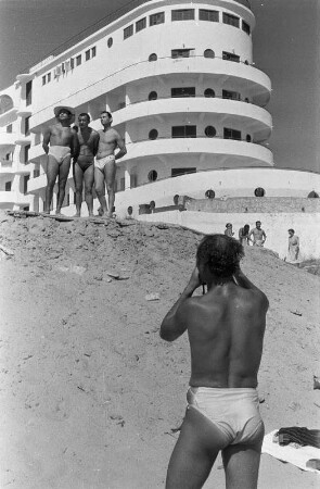 Eforie. Ein Mann fotografiert drei andere Männer am Strand am Schwarzen Meer vor einem Hotel
