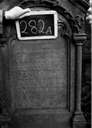 Grabstein 282 (Index: 100112050) Material: Sandstein Zustand: verwittert Maße HxBxT: 190x64x30 cm Beschreibung: ädikulaartige Stele mit Säulen, getreppter Sockel, schräg eingezogener Segmentbogenabschluß mit Mittel- und Eckakroteren, Schriftfeld eingetieft mit Rundbogenabschluß Symbolik: Ranken, Rundbogenfries: Grabstein 282A