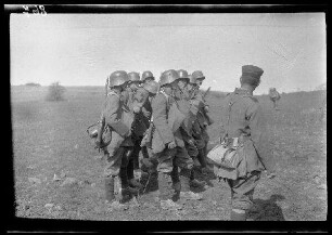 Übungsgelände I bei Mouzon (Dep. Ardennes, Frankreich): 8 Soldaten mit Stahlhelm in 2 Vierer-Reihen hintereinander auf einem kahlen Feld (Seitansicht, Nahaufnahme)