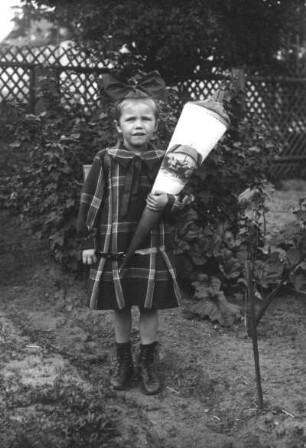 Schulanfängerin mit Zuckertüte im Garten stehend