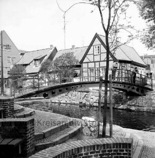 Trave: Stadtarm: Personen auf der Brücke zwischen der Hude und Heiligengeiststraße, vorne Uferterassierung, im Hintergrund Gebäude der Heiligengeiststraße, Blick nach Nordwesten
