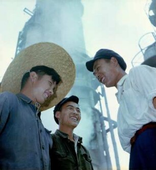 Drei lachende Arbeiter in einer Erdölraffinerie