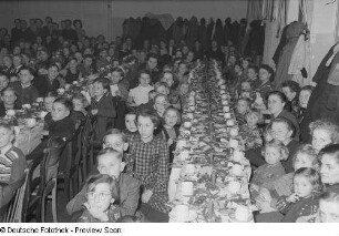 Kinder und Mütter an einer gedeckten und geschmückten Tafel bei der Weihnachtsfeier des Verlags Volk und Wissen