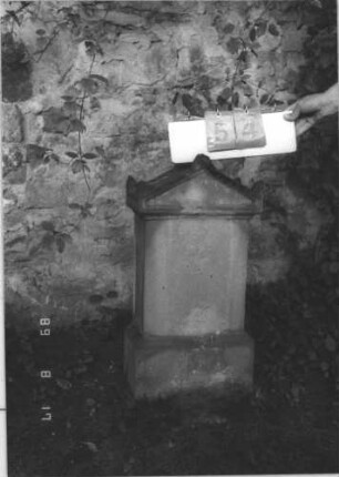 Grabstein 54 (Index: 100105671) Material: Sandstein Zustand: vollständig verwittert Maße HxBxT: 75x40x18 cm Beschreibung: Stele auf Sockel, Giebel mit Akroteren: Grabstein 54