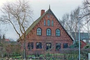 Hauptstraße 31: giebelständiges Bauernhaus aus Backstein: Straßenfront Wohntrakt, oben Rundbogenfenster, Giebelzier, unter Ortgang Backsteinfries: an Traufseite links kleiner Querbau, rechts Nebengebäude: im Vordergrund Feldsteinmauer, Hecke
