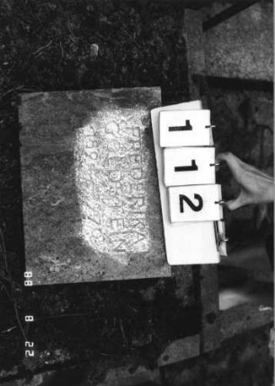 Grabstein 112 (Index: 100080306) Material: Kunststein? Zustand: leicht verwittert Maße HxBxT: 44x33x6 cm Beschreibung: schräg aufgestellte Bodenplatte: Grabstein 112