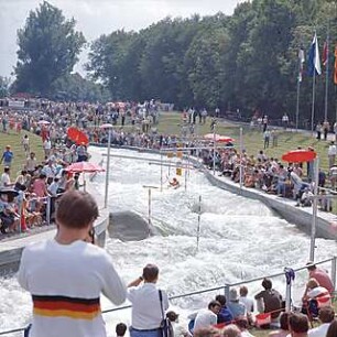 Hansjakob, Gottfried; Augsburg - Spickel, Am Eiskanal 30A; Kanuslalom Olympiastrecke, Freiflächengestaltung - Kanustrecke, Kanute beim Training mit Slalomtoren, Tribünen mit Zuschauern
