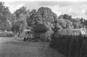 Reinbek: Mühlenteich: Blick von Schlossstraße Richtung Nordosten auf gegenüberliegendes Ufer: vorn Mitte Pavillon in Garten: dahinter und links Geländer: links Einmündung der Bille, Ruderboot: hinten rechts Schwäne im Wasser: hinten Bäume und Rasenfläche