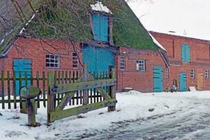 Dorfstraße (15): traufständiges Fachwerkhaus mit Reetdach: Giebelseite Wirtschaftstrakt mit Stalltüren, Scheunentor, darüber Luke: hinten rechts rückwärtiger Stallquerbau: Hof, vorne Lattenzaun, Gatter, Einfahrt