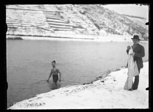 Schwimmer im Main am schneebedeckten Ufer ein Mann in Jacke und Hut mit Handtuch oder Bademantel in der Hand