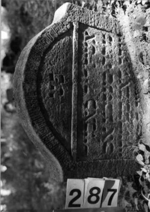 Grabstein 287 (Index: 99803431) Material: Sandstein Zustand: verwitt/eingesunk(befestigt)/Textverlust Maße HxBxT: 48x60x9 cm Beschreibung: Stele mit Karniesbogen und profiliertem Rand, Giebelfeld: Grabstein 287
