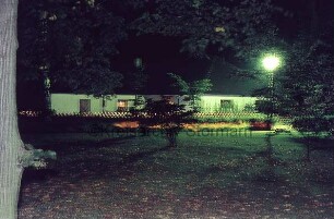 Kurpark: Tennis- und Hockey-Club Blau-Weiß e.V.: davor Jägerzaun: vorn Rasen, Büsche, Bäume, Straßenlampe: Nacht