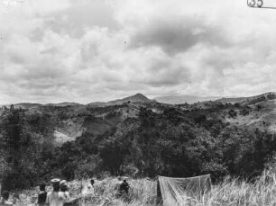 Landschaft : Blick von einer Anhöhe in das bewaldete Tal und auf die bergige Umgebung. Im Vordergrund ist ein Teil des Lagers der Forschungsreisenden erkennbar