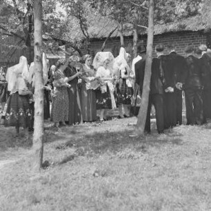 Sorbische Hochzeit in Burg-Kauper. Hochzeitsgäste auf dem Hof des Brautpaares Werchosch bilden ein Spalier zur Verabschiedung des Brautpaares. : Serbski kwas w Kupaŕskich Bórkowach. Kwasarjo na Wjerchošec dworje tworja spalěr k rozžohnowanju njewjesćinskeho porika.