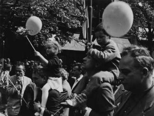 Kinder mit Luftballons auf den Schultern Erwachsener beim Umzug am 1. Mai