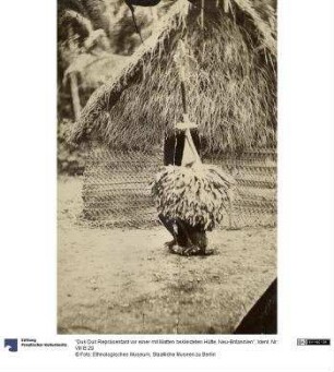 "Duk Duk Repräsentant vor einer mit Matten bekleideten Hütte, Neu-Britannien"