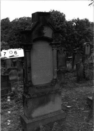 Grabstein 706 (Index: 100099638) Maße HxBxT: 188x55x21 cm Symbolik: Blumenkranz Besonderheit: kulturhistorisch wertvoll / hist.-wiss. Gründe (Gemeindestellung): Grabstein 706
