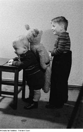 Zwei Kinder, eines spielt mit einem Teddybären