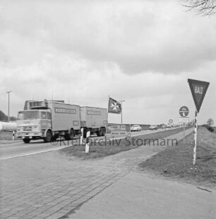 Nütschau: Malteser Hilfsdienst e.V.: Bundesstraße B 404: vorn Einmündung der Schlossstraße mit Verkehrsschildern und Flagge mit Malteser-Kreuz: dahinter Lkw mit Anhänger und Pkws
