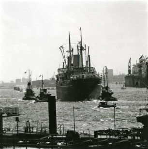 Hamburg. Hafen. Ein Frachtschiff wird von Schleppern aus dem Hafen bugsiert.