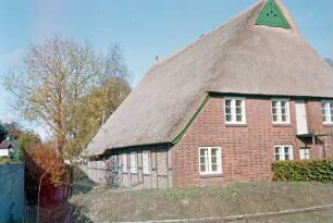 Reinbeker Straße 4a: giebelständige Fachwerkkate mit Reetdach: rückwärtige Giebelseite Wohntrakt mit Sprossenfenstern, Türen, oben Giebelzier, Eulenlöcher: Traufseite, von rechts Wohntrakt, Sprung, Wirtschaftstrakt: im Vordergrund Hecke, Neuaufschüttung Wall, Absperrband