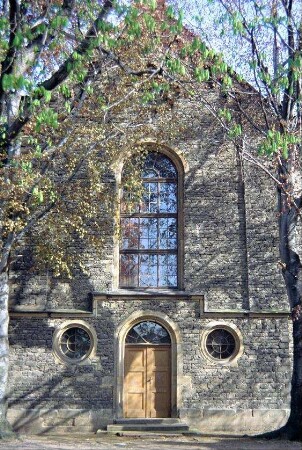 Giebelfront der Kirche mit Eingangstür an de Südseite; großes Rundbogenfenster über der Tür