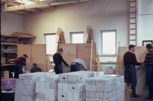Kreisberufsschule [Ahrensburg]: Hermann-Löns-Straße: Innenaufnahme: Unterrichtsraum für Maurer: Auszubildende, Anleiter, im Vordergrund Stapel mit Mauersteinen