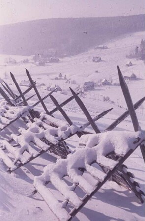 Blick auf eine Ortschaft im Erzgebirge im Winter, mit Schneezäunen im Vordergrund