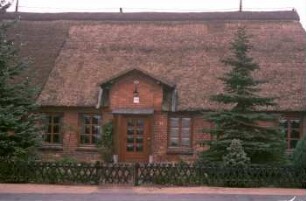 Dorfstraße 33: traufständige Backsteinkate mit Reetdach: Straßenfront, Teilansicht: Fenster mit Butzenscheiben, Eingangstür, darüber Zwerchgiebel: Vorgarten, Jägerzaun