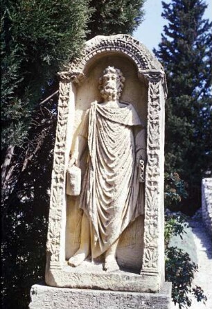 Stele mit männlicher Gewandfigur eine Panflöte in der linken Hand haltend