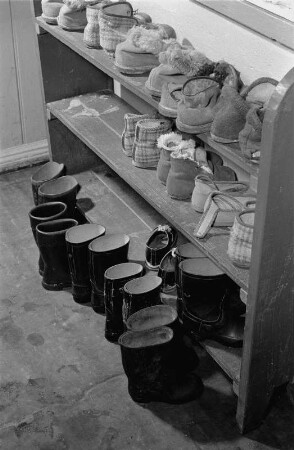 Landflucht. Schuhregal mit Hausschugen und davor abgestellten Gummistiefel (wohl im Lehrlingswohnheim in Trinwillerhagen)